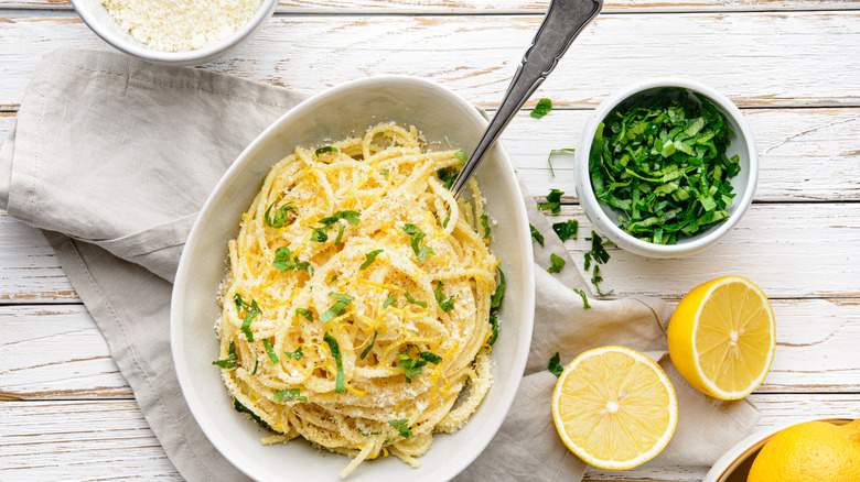 Spaghetti with Parmesan, butter, and lemon sauce in a white bowl, topped with chopped parsley, fresh grated zest, and cheese on rustic wooden background