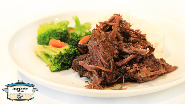 Slow cooked beef next to steamed carrots and broccoli on a white plate