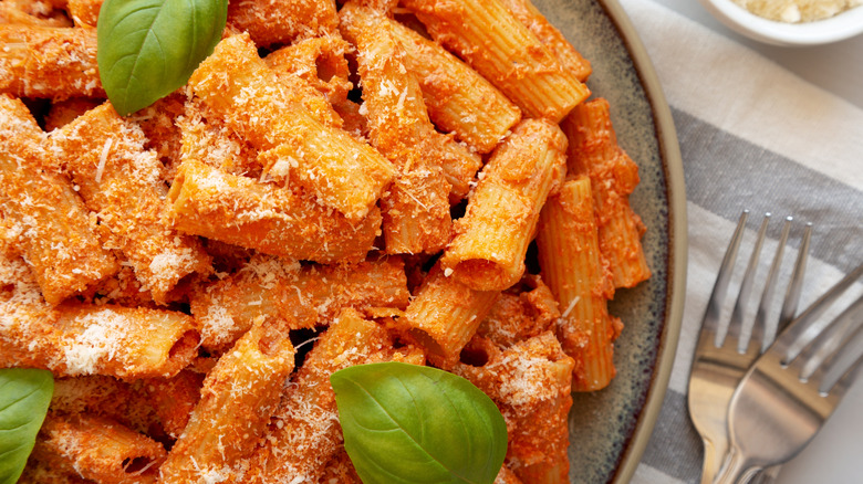 Close up of a bowl of penne in vodka cream sauce with basil leaves and grated parmesan