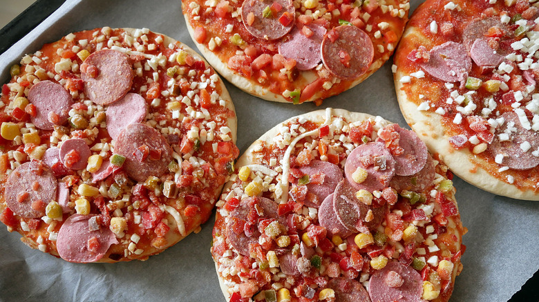 A cooking tray with four small frozen pizzas waiting to be baked.