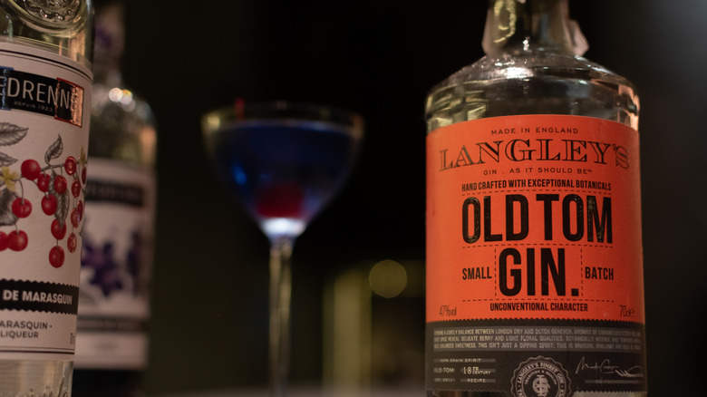 A bottle of Old Tom Gin next to a bright blue cocktail with a cherry
