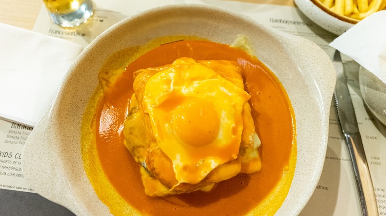 Traditional Portuguese Francesinha sandwich served on a restaurant table, topped with melted cheese and savory sauce, capturing authentic Porto cuisine and dining culture.