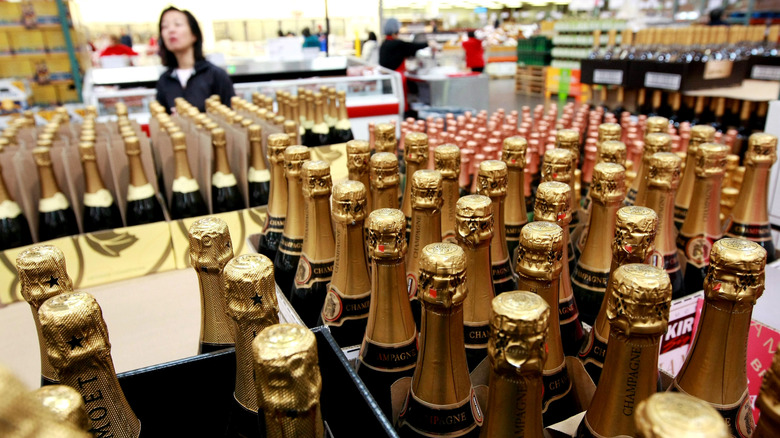 A woman looking over stacks of champagne with gold foil tops at a Costco