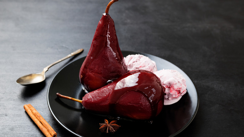 Stewed purple pears in a wine reduction syrup with ice cream on a black plate
