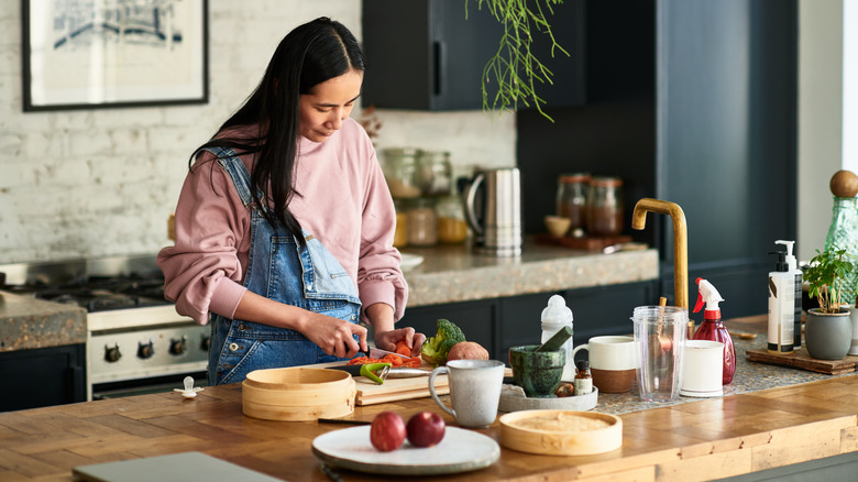 A woman standing in the kitchen cutting vegetables and cooking