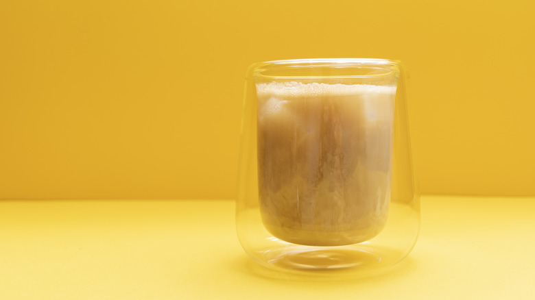 dirty soda in a glass against a yellow background