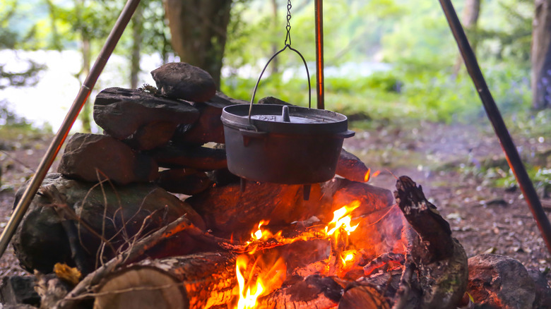 A cast iron pot hanging over a campfire by a chain.