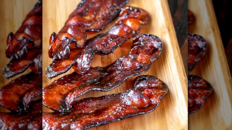 A closeup of candied bacon strips on a wooden platter