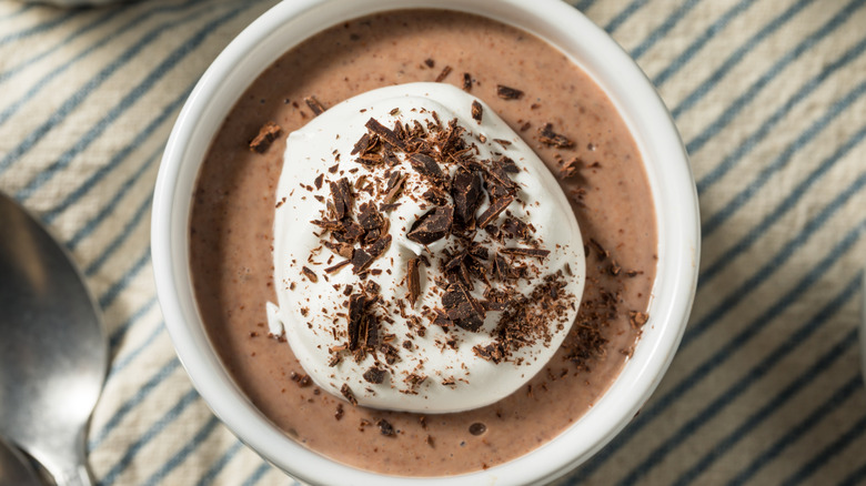 Chocolate pudding in a small, white bowl with whipped cream and chocolate shavings