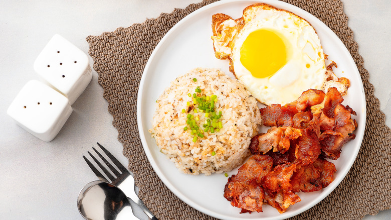 Top view of Filipino Sinangag garlic fried rice with fried eggs and bacon