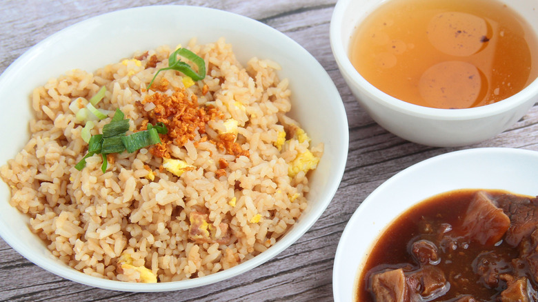 Sinangag rice in a white dish next to a bowl of broth and a bowl of sauced roasted beef