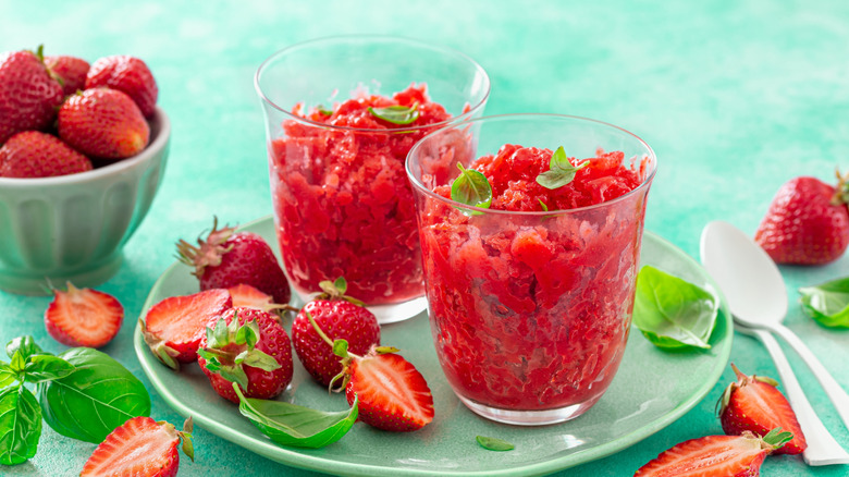 Two glasses with red granita on a round green plate surrounded by strawberries