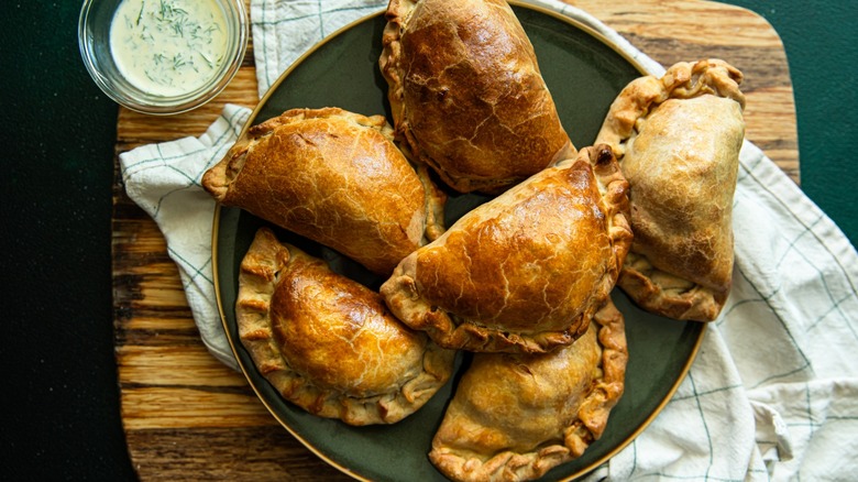 Homemade empanadas on green plate with dipping sauce nearby