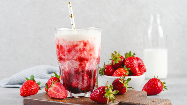 Milk and strawberry puree in glass with straw and berries on side