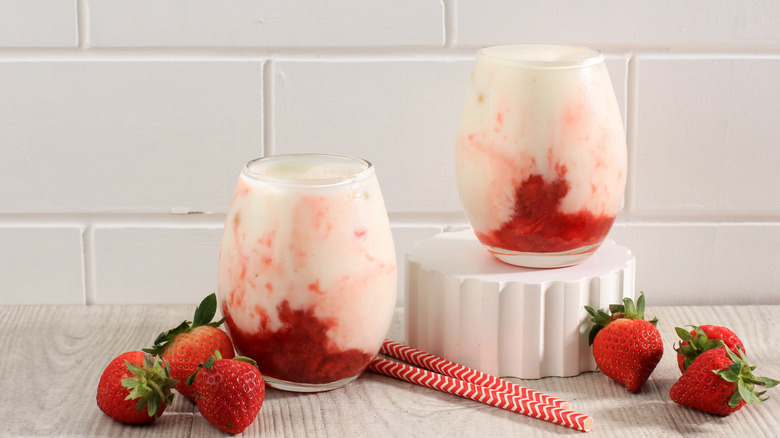 Two cups of Korean strawberry milk next to some whole strawberries