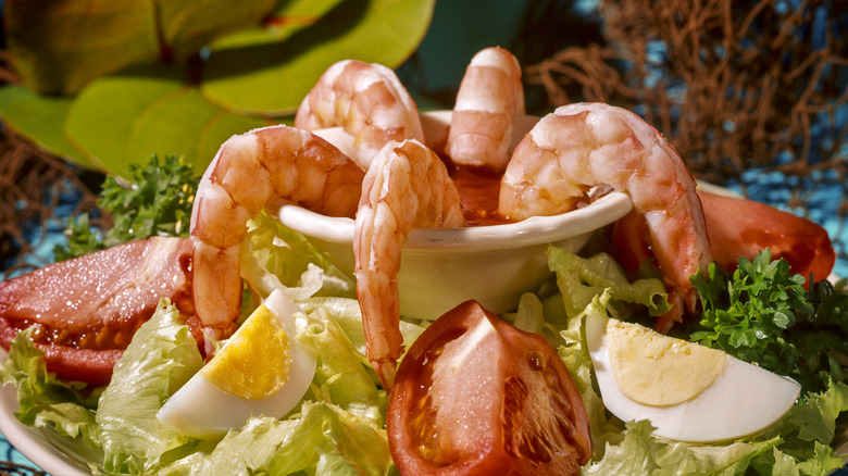 Shrimp in cocktail sauce in retro-style plating with tomatoes and egg slices.