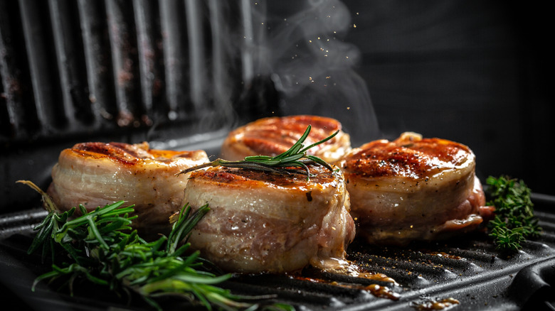 Four portions of bacon-wrapped filet mignon on a grill