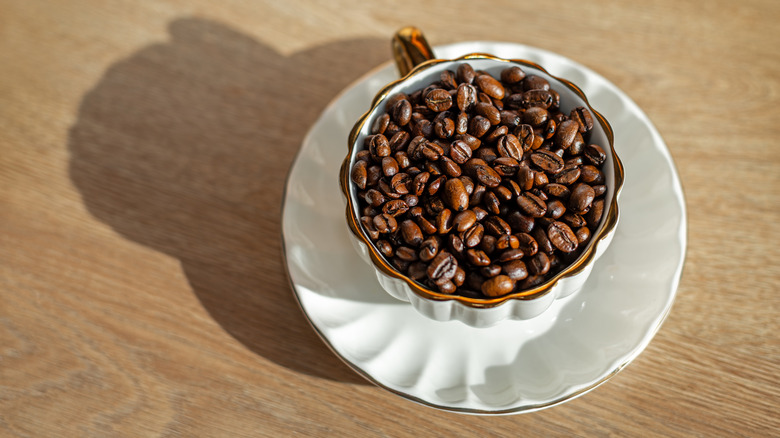 Coffee beans inside a mug outside in the sunlight on a wooden surface