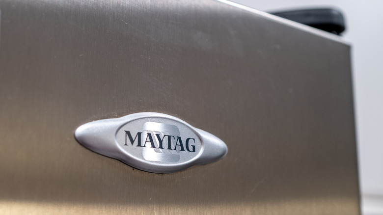 A close up of maytag logo on corner of stainless steel refrigerator