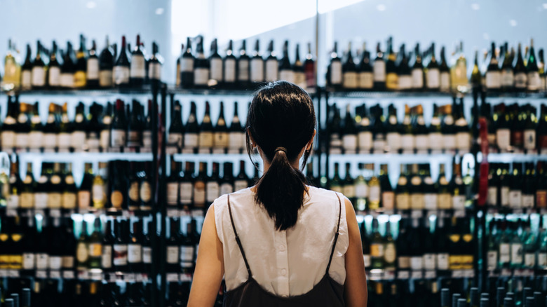 A woman selects wine on shelves in a grocery store