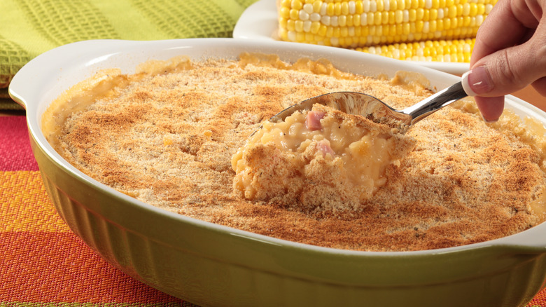 Spoon takes a scoop out of a creamy corn casserole dish topped with bread crumbs