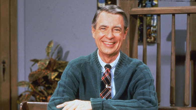 Mister Rogers smiles at the camera in the house on the set of his TV show in cardigan and tie