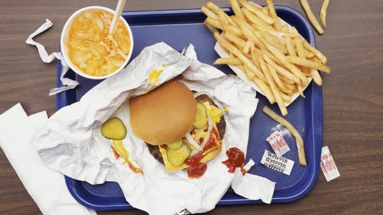 a blue tray with a drink, fries, and a burger with cheese, mustard, ketchup, onions, and pickles