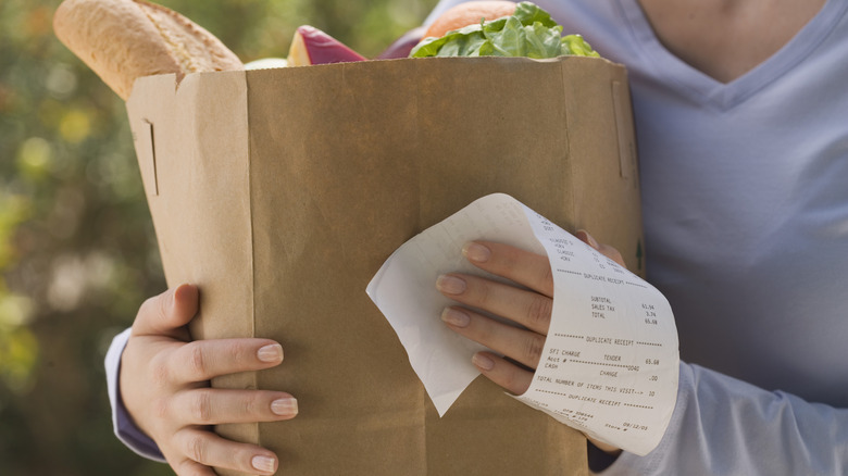 Person holding full paper grocery bag and receipt