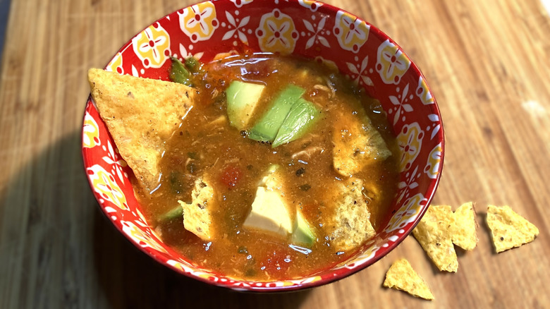brightly colored bowl full of Kirkland Signature Chicken tortilla soup topped with corn chips and diced avocado pieces