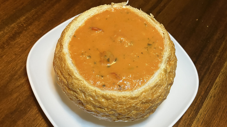 chunky tomato soup with flecks of herbs in a bread bowl on a white plate