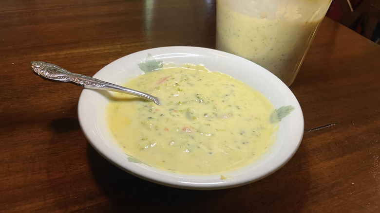 A bowl and a clear plastic container, both full of broccoli cheese soup