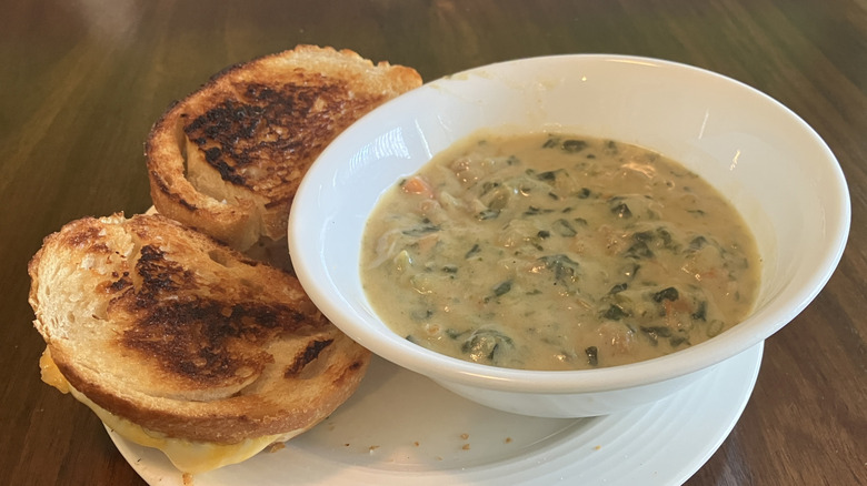 Grilled cheese sandwiches on a plate next to a bowl of Ivar's Rustic Zuppa Toscana soup with lots of bits of spinach in it