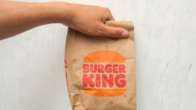 A person holding a paper Burger King bag.