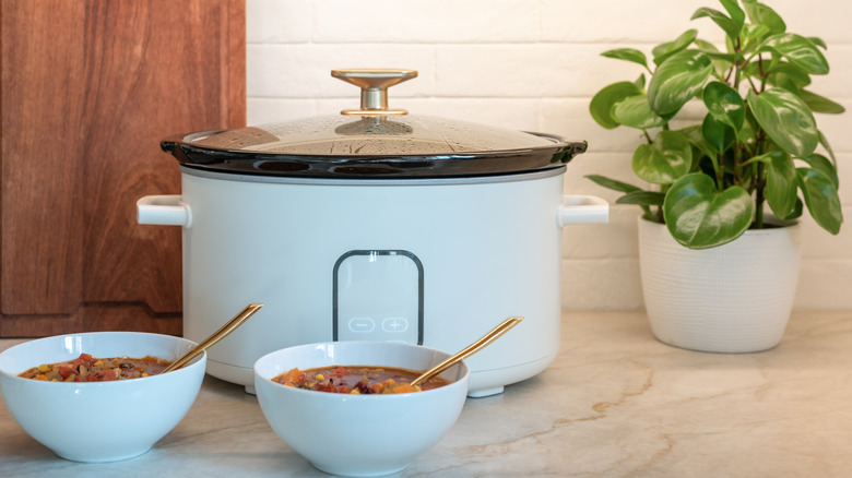 White slow cooker and two bowls of food sitting on a kitchen counter.