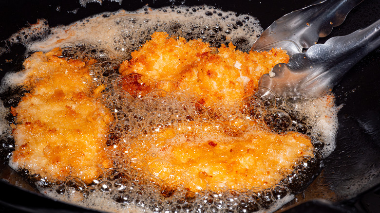 Three pieces of breaded fried chicken sizzle in an oil filled pan