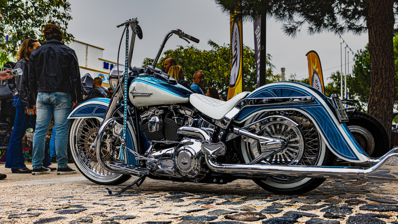 A blue and white Harley-Davidson motorcycle sitting on cobblestone with bikers hanging out in the background in Portugal.