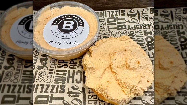 Bagel halved and spread with honey sriracha cream cheese with a container of honey sriracha cream cheese beside it at Bad Guy Bagels