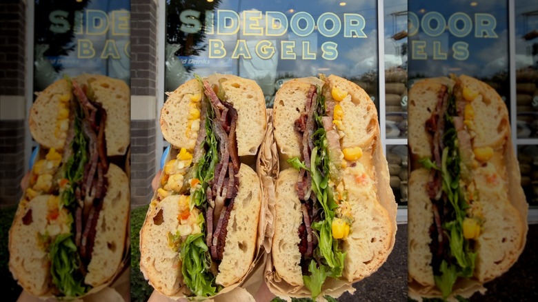 Loaded bagel sandwich in front of front door with window showing name logo at Sidedoor Bagels