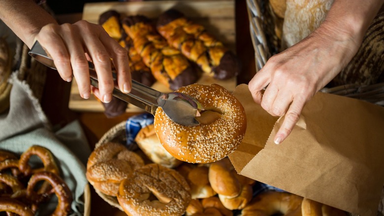 Picture of a staff worker hand placing a bagel in a takeaway bag at a bakery bagel shop