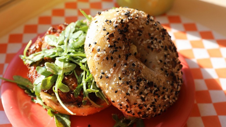 vegan bagel sandwich with veggie patty, pickled onions, arugula, vinaigrette, and vegan veggie cream cheese on everything bagel at Know Good Bakery
