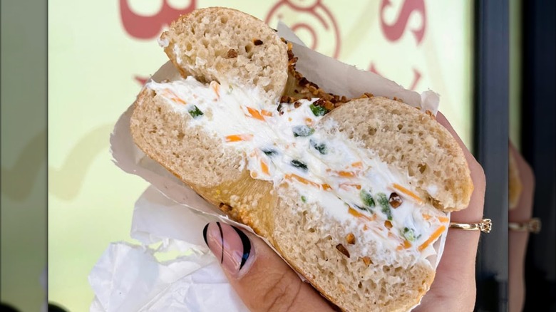 hand holding a Garlic bagel filled with a lot of veggie cream cheese at Abel's Bagels