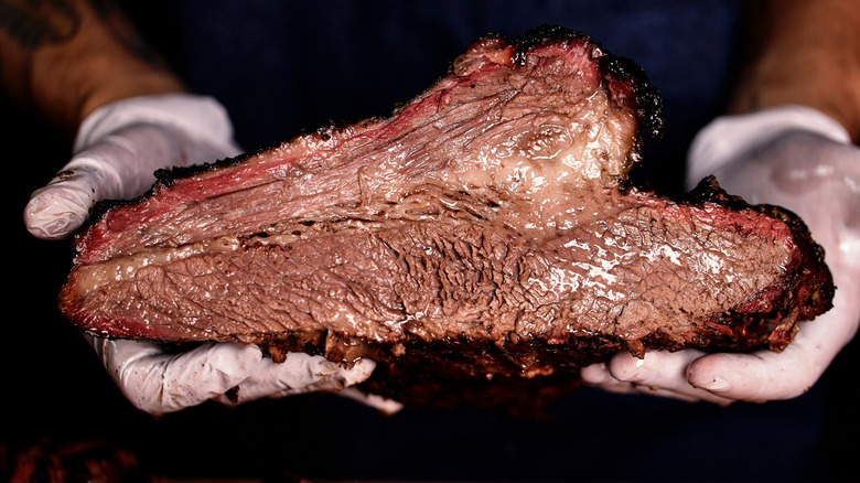 Hands holding a whole smoked brisket