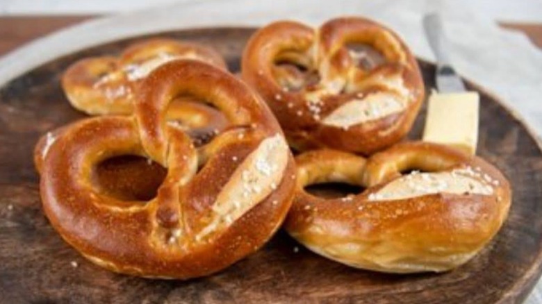Stack of soft pretzels on a wooden board with a pat of butter