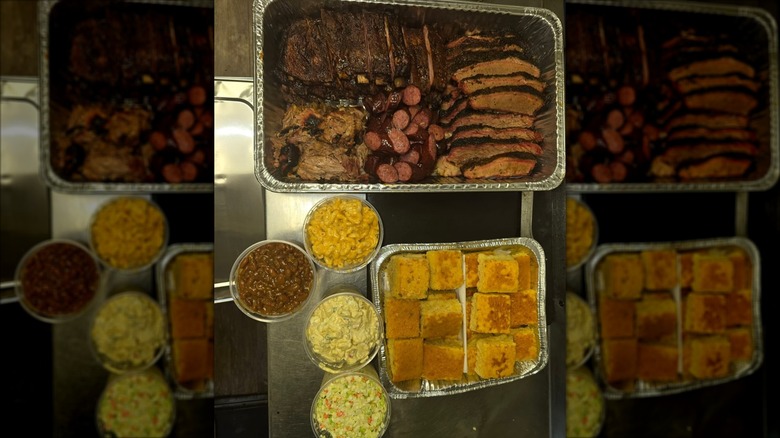 Assorted barbecued meat in an aluminum pan served with sides of cornbread, corn, beans, and coleslaw