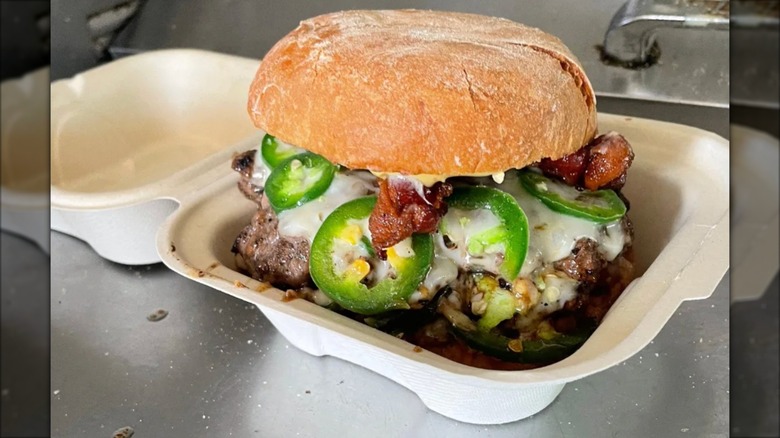 Smashburger with jalapeños, bacon, and cheese in a to-go container