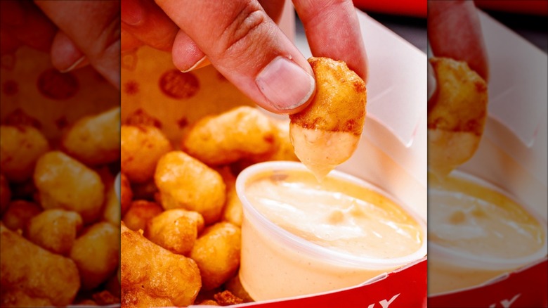 Container of cheese curds being dipped into a sauce