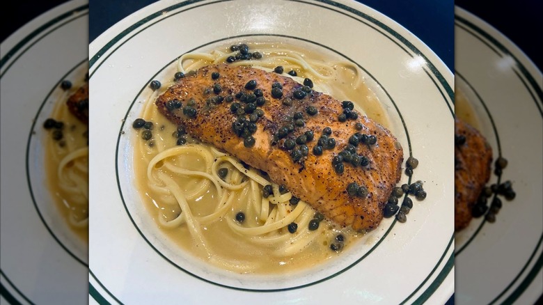 Grilled salmon fillet plated over linguine with lemon butter caper sauce
