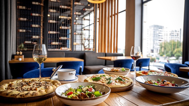 Bright modern restaurant interior with Italian pizza, pasta, salad and wine on a wooden table
