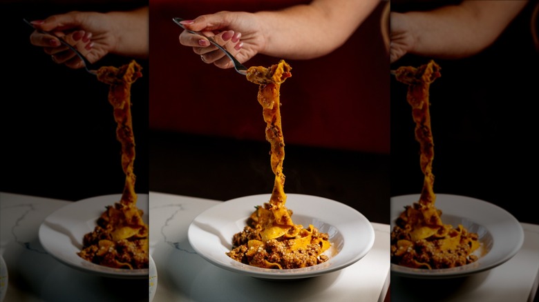 hand shown with a forkful of pappardelle pasta in bolognese sauce with parmesan and rosemary from Pulito Osteria