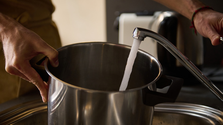 Hands filling a pot with tap water